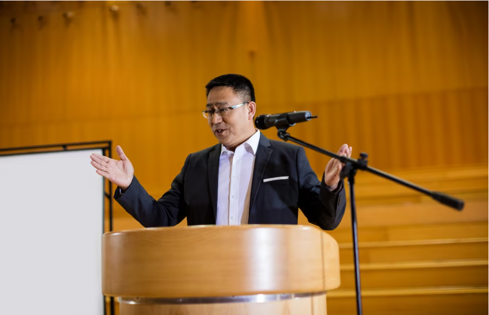 An image of an Asian speaker using persuasive techniques to deliver his speech and influence his audience