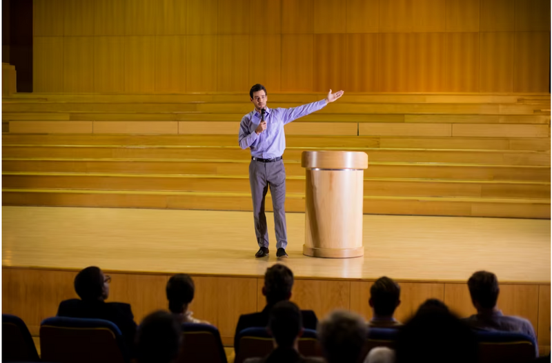 A featured image featuring a speaker showcasing his public speaking techniques before an audience